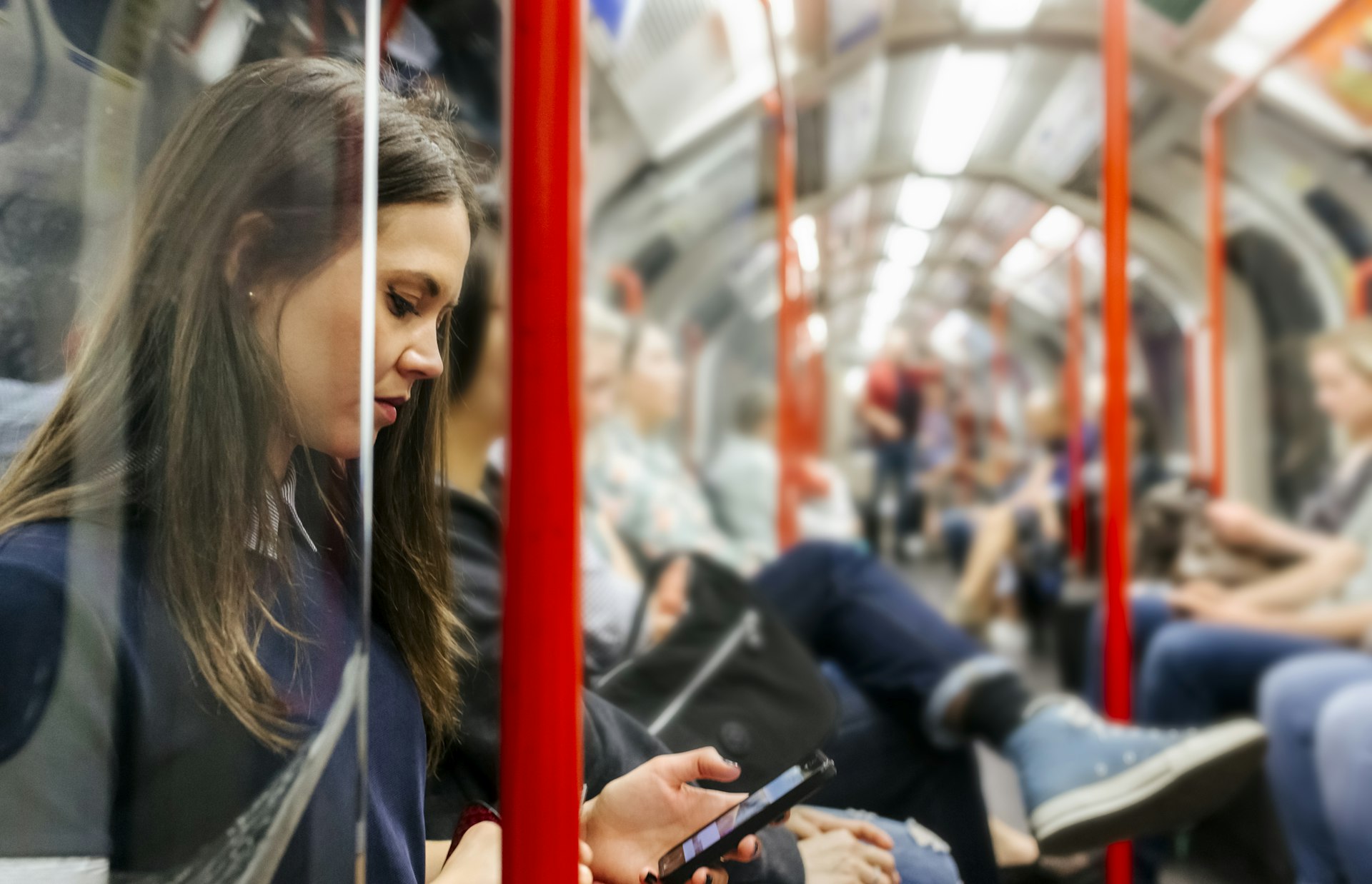A side view of a woman sitting on the London tube looking at her phone