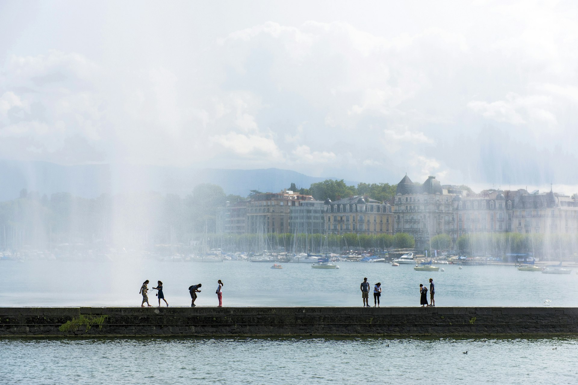 People on the edge of a lake are sprayed with the mist of a vast jet of water shooting into the air