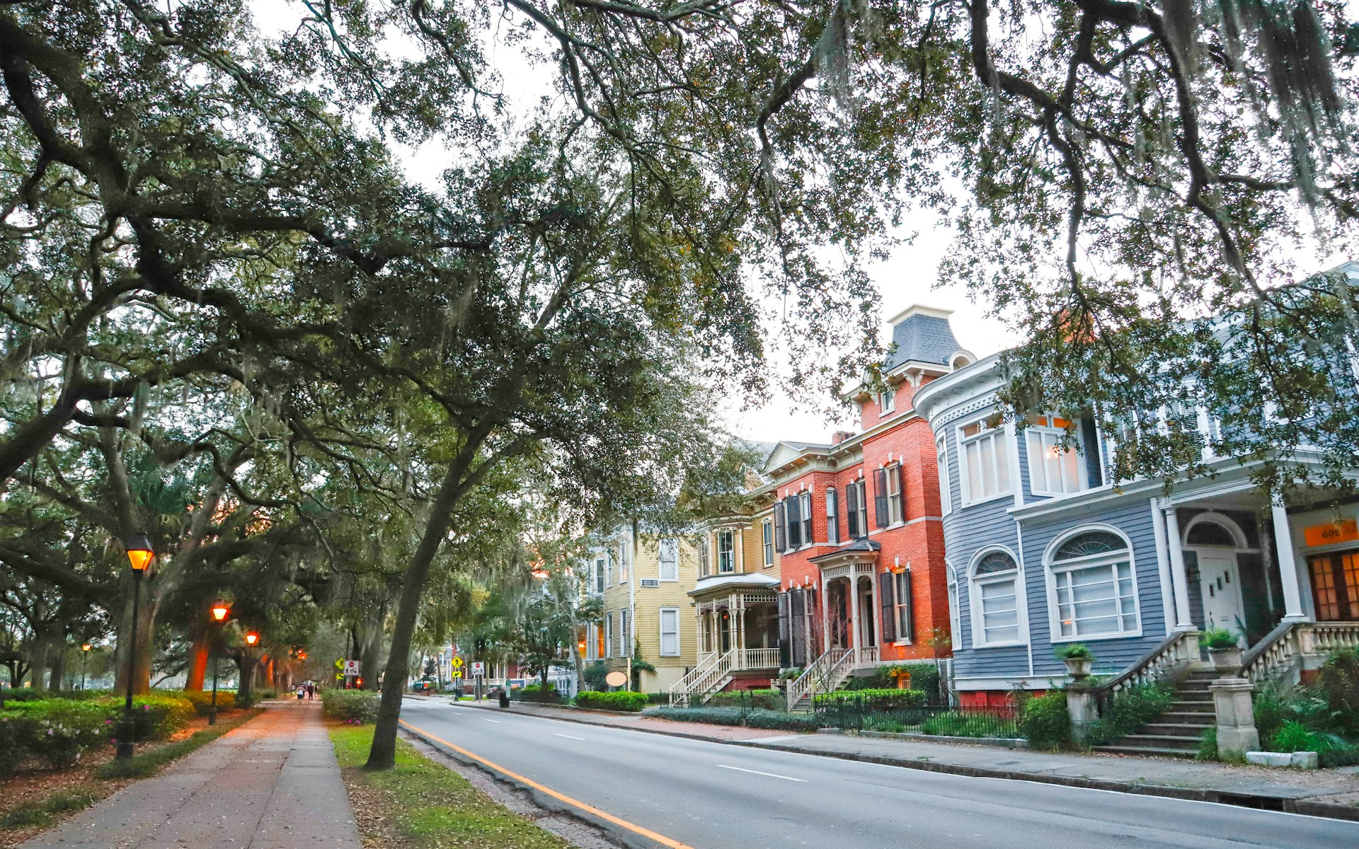 Several candy-colored historic homes sit along a street at dusk in Savannah, Georgia
