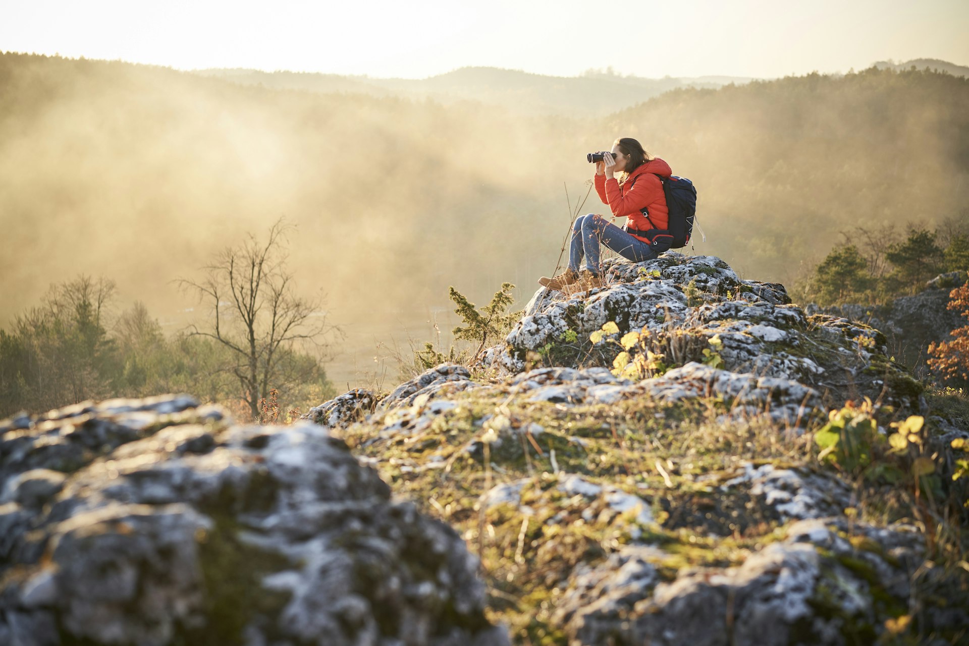 Woman on a hiking trip in the mountains sitting on a rock looking through binoculars in Poland