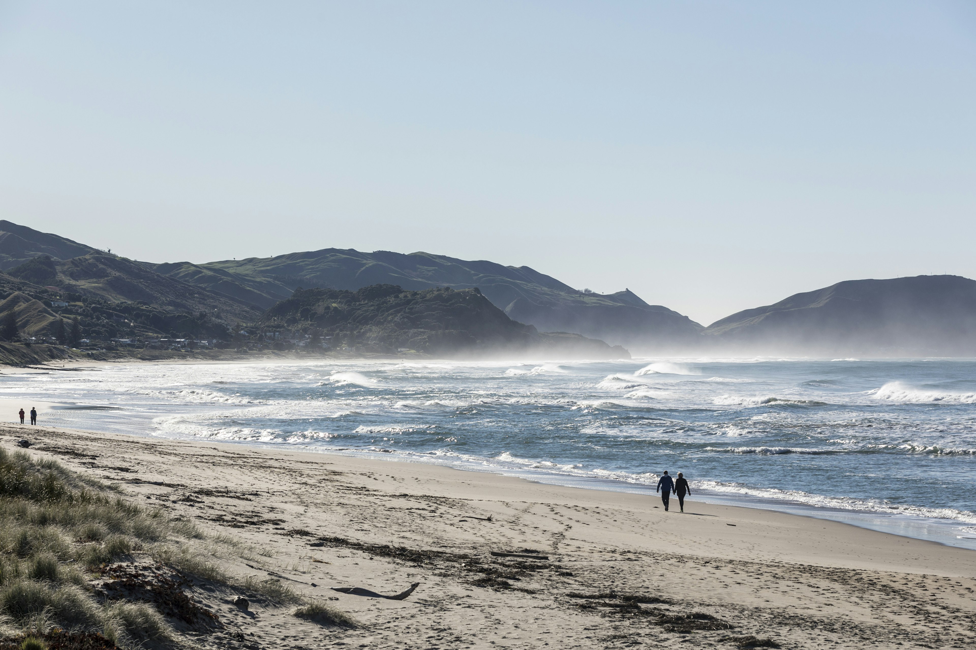 People in silhouette as they stroll along a beach with big waves