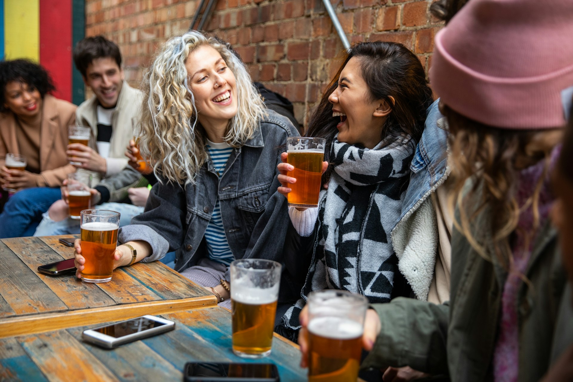 A group of friends at a pub laugh while holding pints of beer