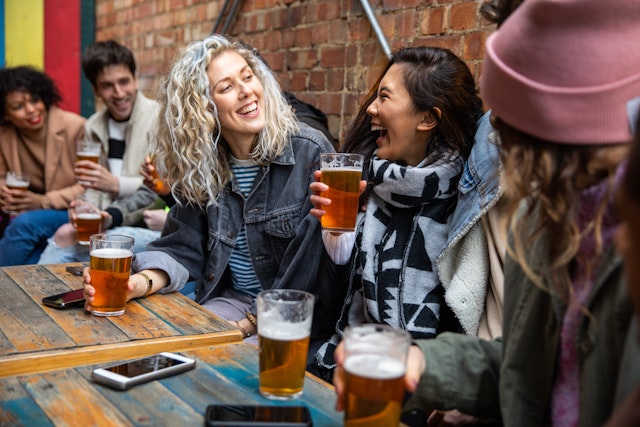A group of friends at a pub laugh while holding pints of beer