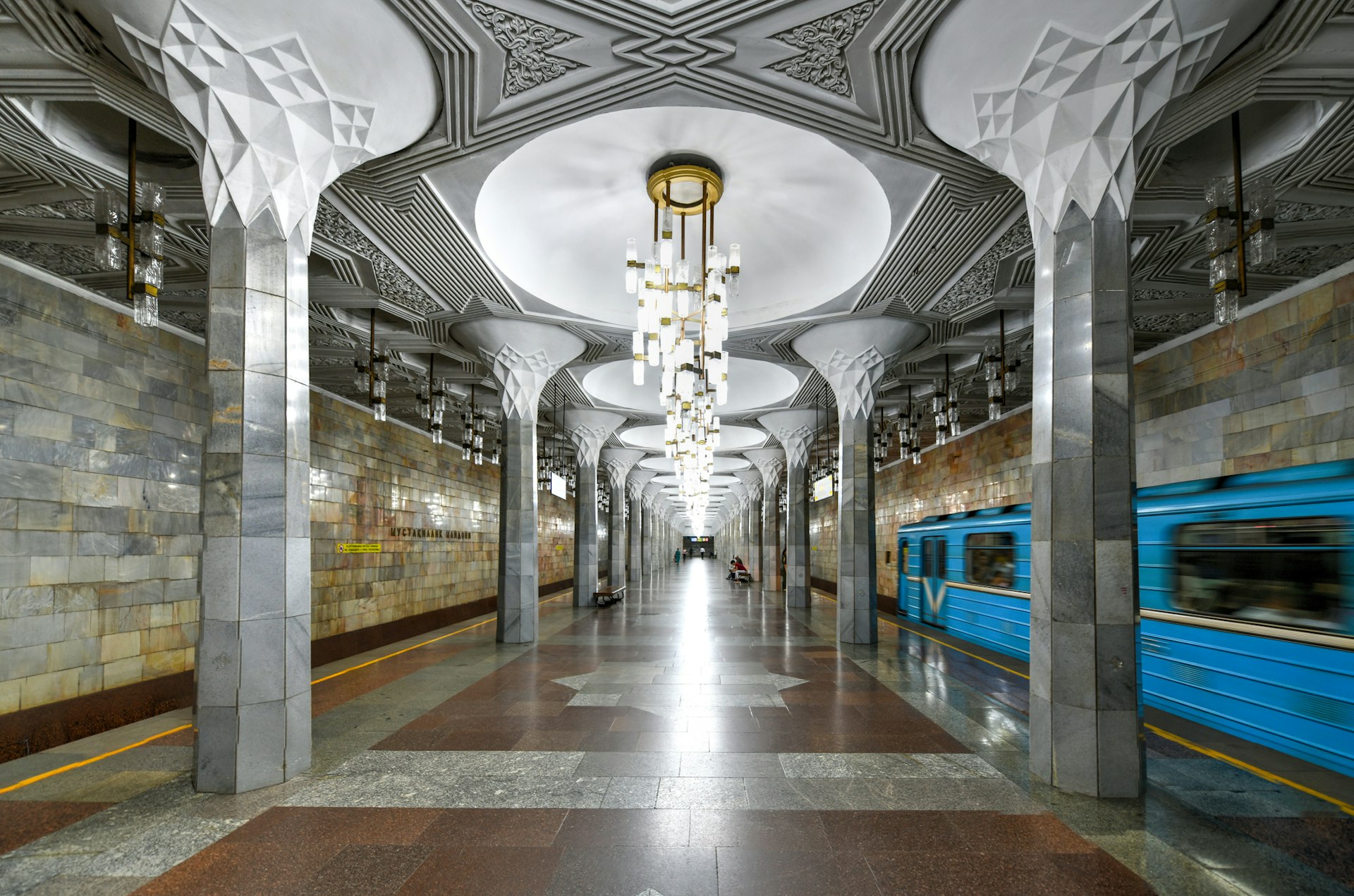 A central platform in an underground station with large decorative light fixtures hanging down