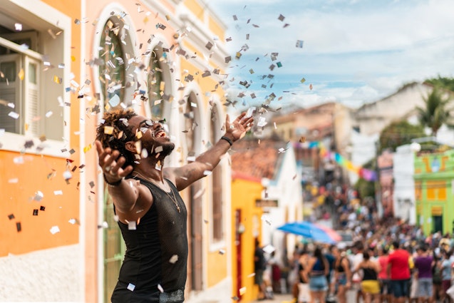 A man throwing confetti in the air at a street party in Olinda, Brazil
