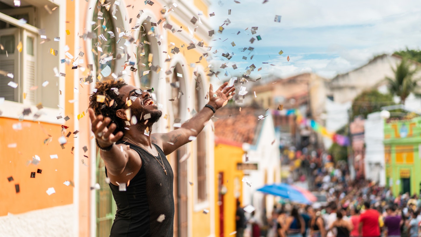 A man throwing confetti in the air at a street party in Olinda, Brazil