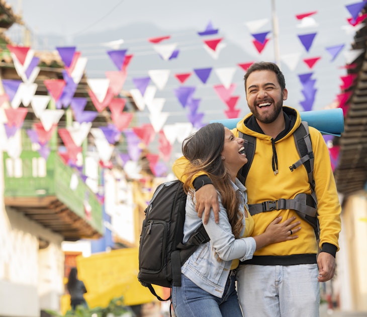 A man and woman embracing and laughing as they walk along a city street in Colombia