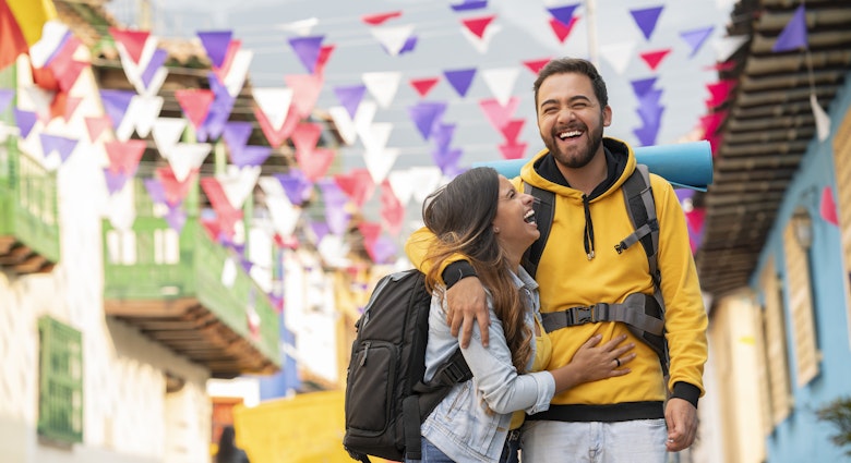 A man and woman embracing and laughing as they walk along a city street in Colombia