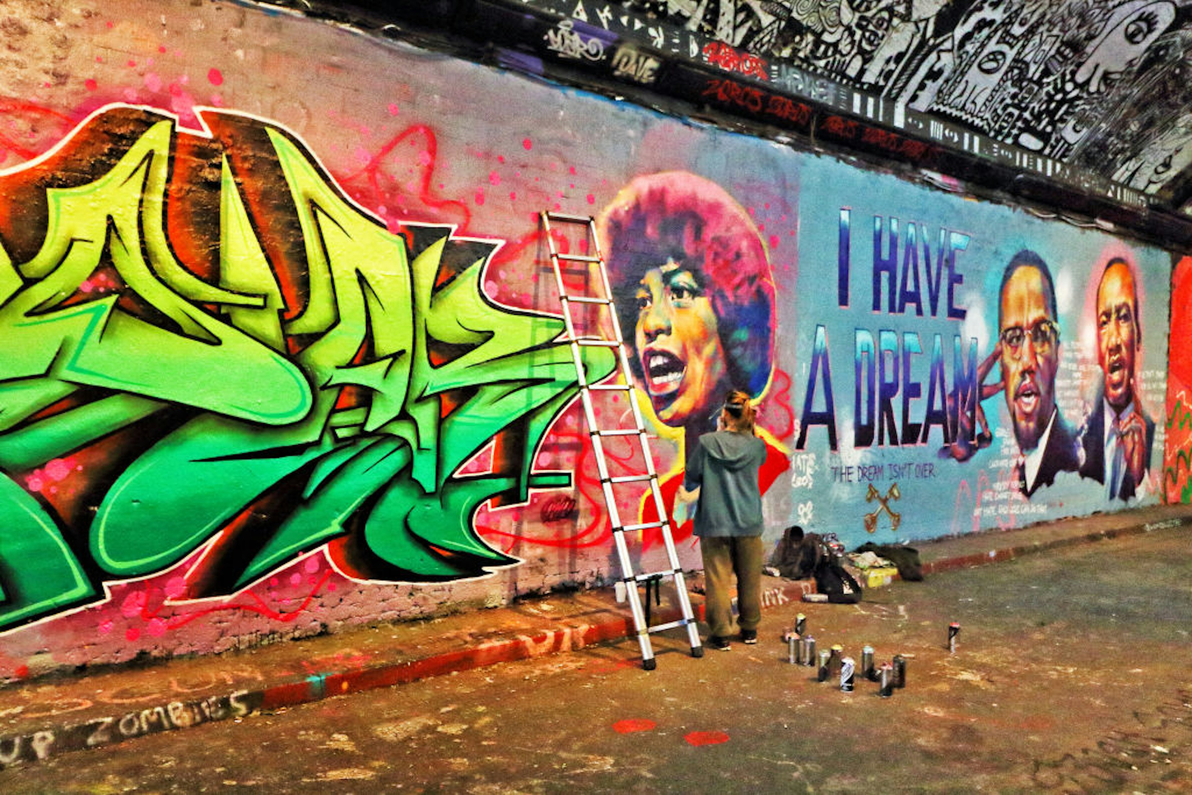 A street artist adds to colorful murals all over a wall in a tunnel covered in graffiti