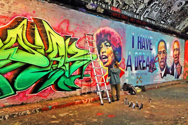 A street artist adds to colorful murals all over a wall in a tunnel covered in graffiti