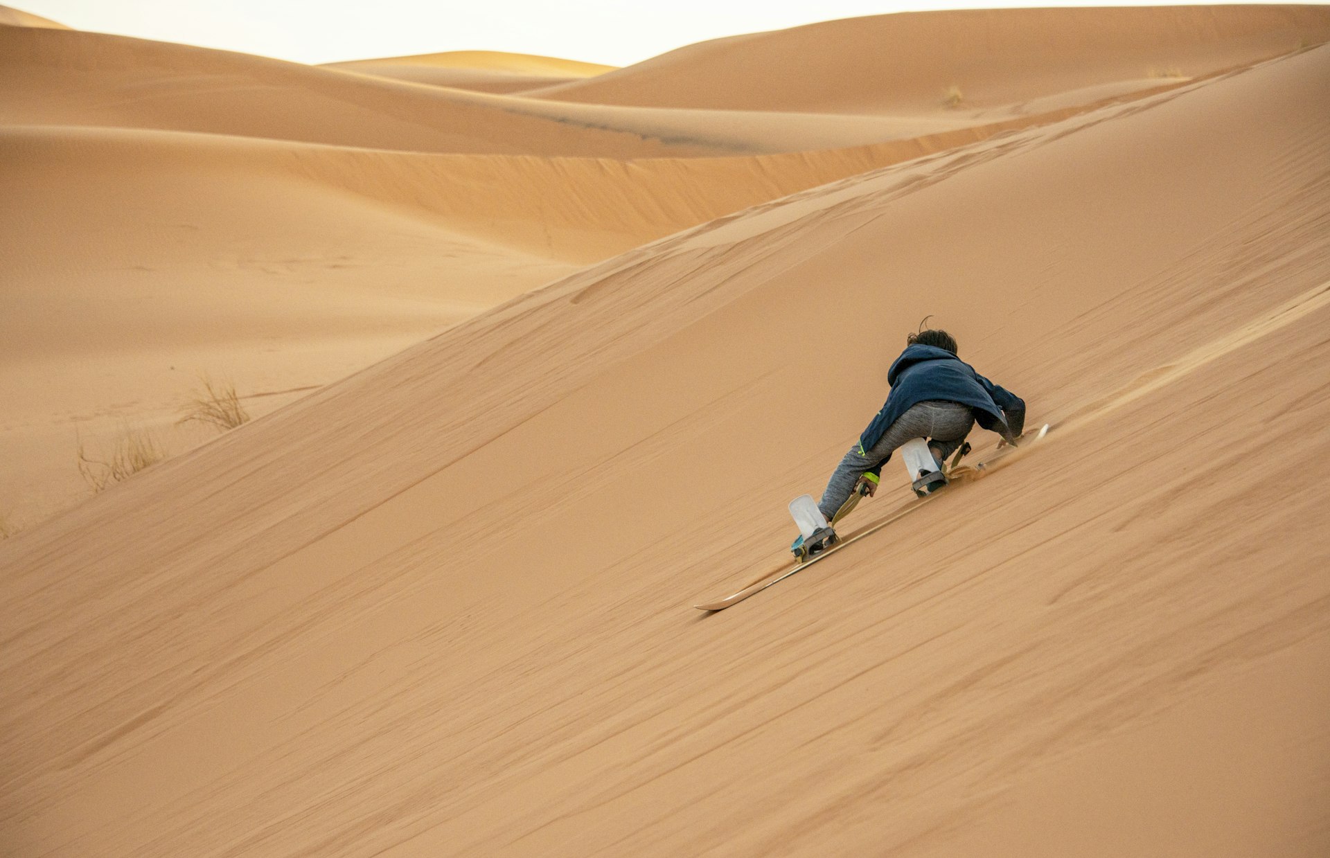 A young boy sandboards down a large dune in the Saraha, Morocco
