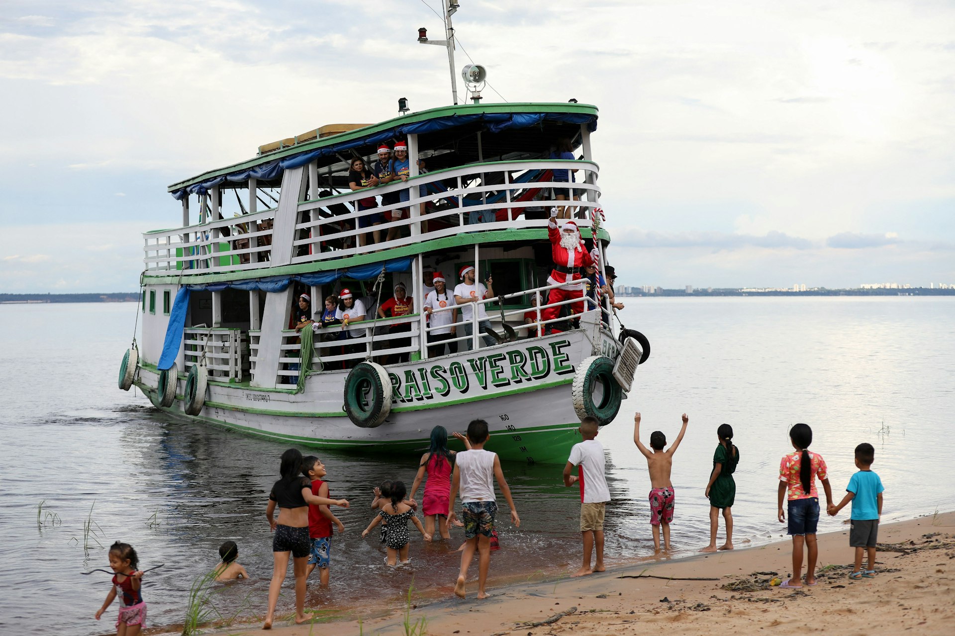 Children from the Iranduba riverside community welcome a boat with “Santa Claus” in Manaus, Amazonas, Brazil