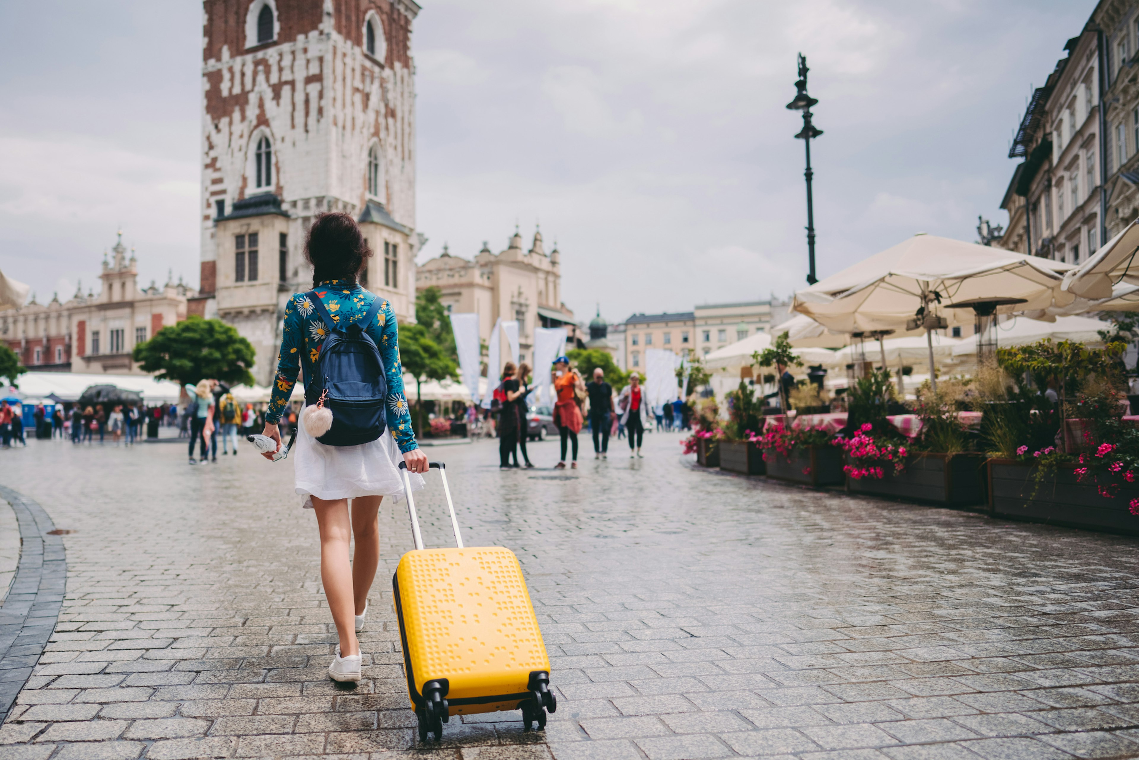 A woman walking through a medieval square in Kraków with a suitcase