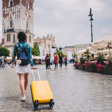 A woman walking through a medieval square in Krakow with a suitcase