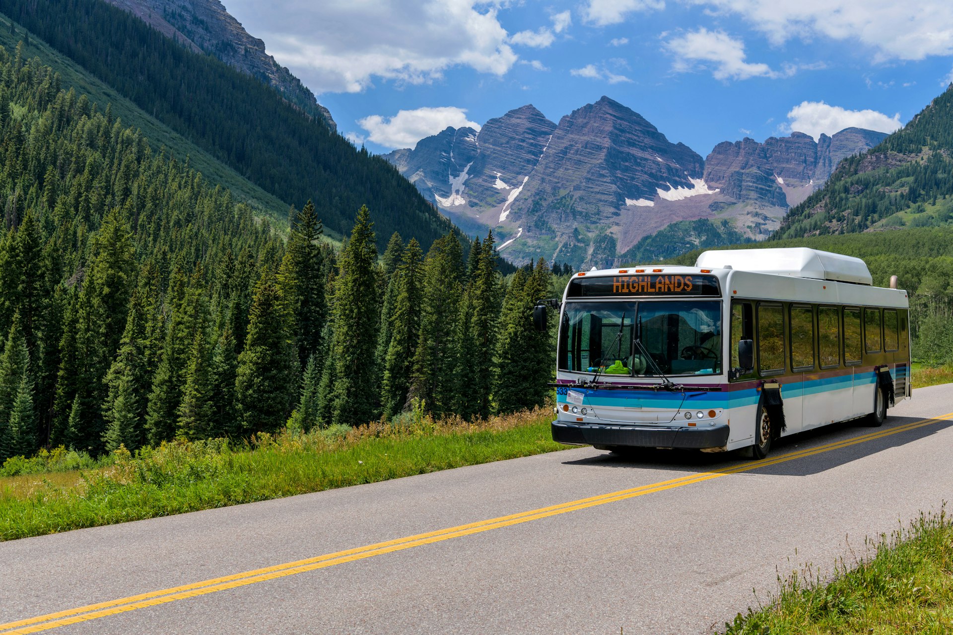 A bus drives a mountain road surrounding by lovely alpine scenery