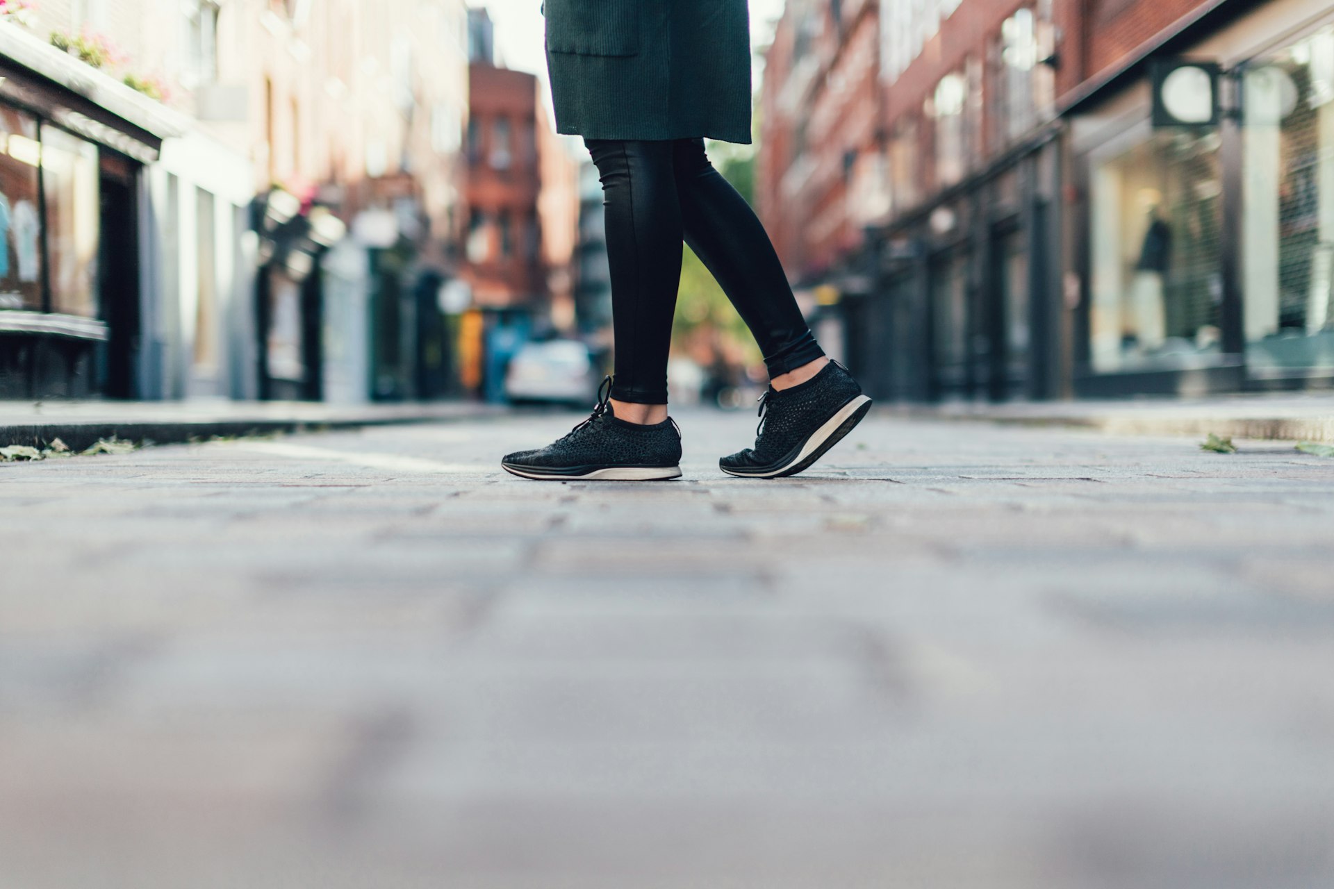 A knee-down shot of a woman walking across London streets in black tennis shoes