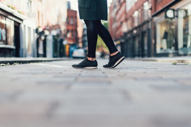 A knee-down shot of a woman walking across London streets in black tennis shoes