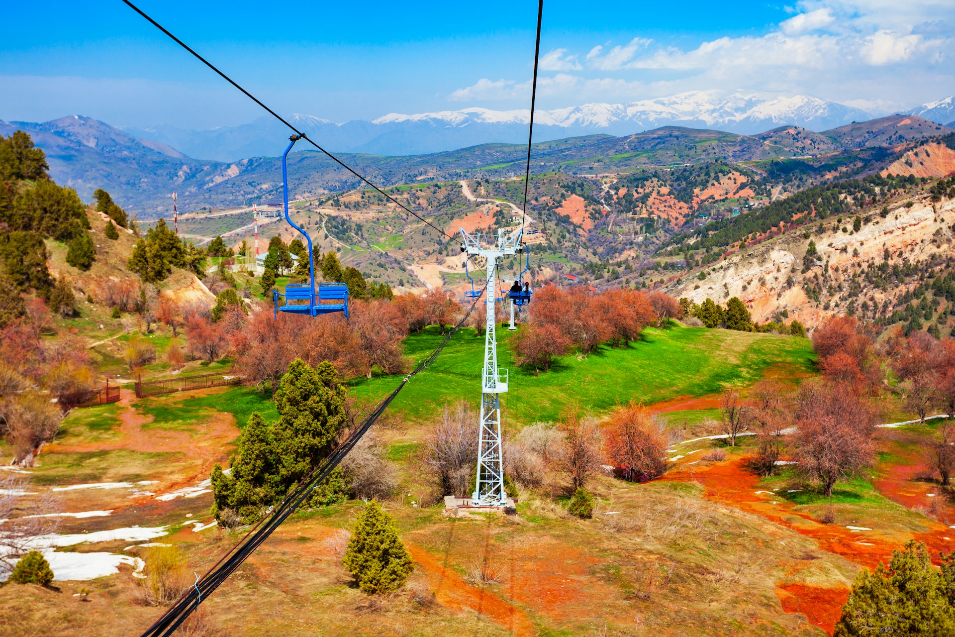 An aerial view of people riding a sky tram into a green valley framed by mountains in Uzbekistan