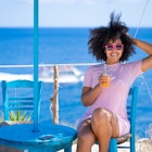 Smiling young woman with sunglasses resting, drinking fruit juice on a beach, sitting on a blue wooden chair
1373066341
A smiling young woman drinking a cocktail at a taverna by the sea in Greece