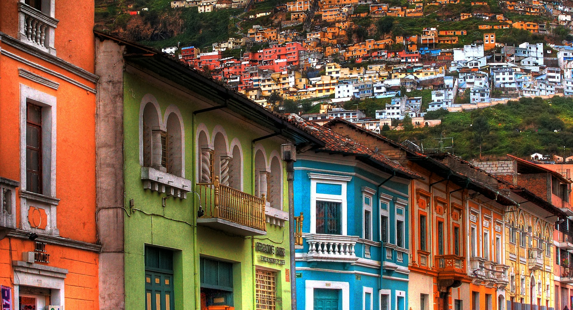 Brightly colored historic homes sit in the foreground with the city of Quito rising on the hillside behind them