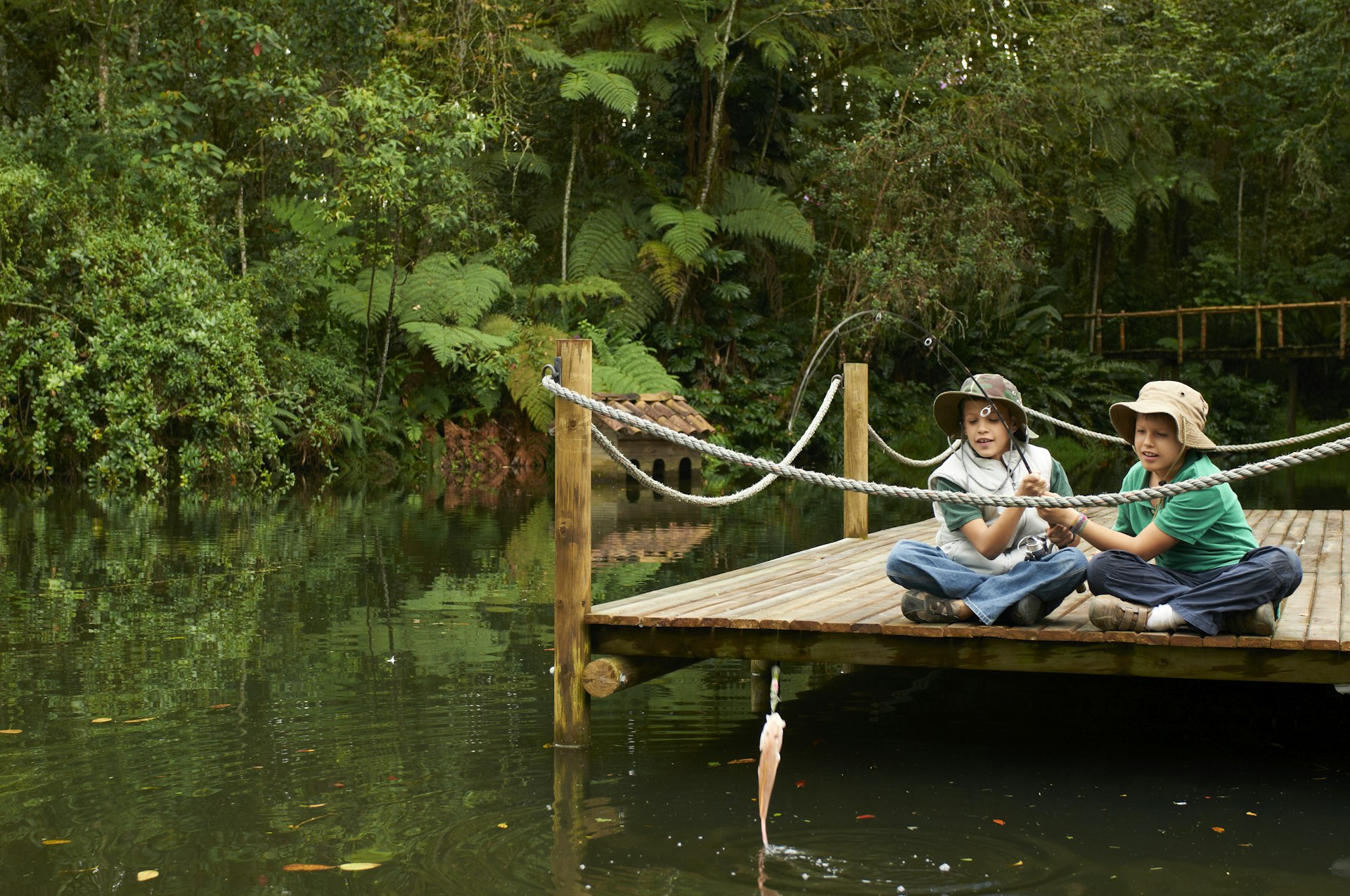 Two young boys fish on a pier in a forested area of Colombia