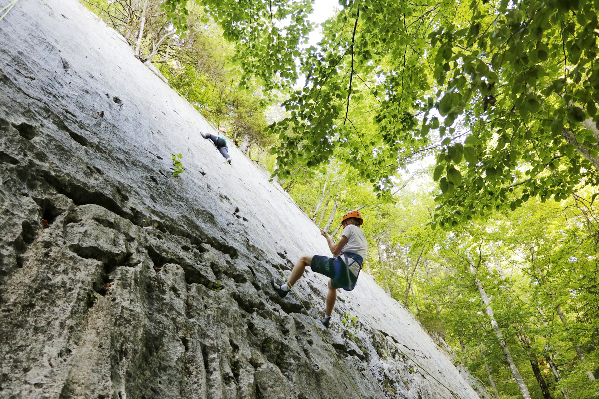 Teenagers rock climbing in the Jura mountains, seen from below as they rappel up a rock face