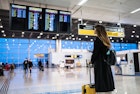 A woman with a suitcase looks at digital screens in an airport in Brazil
