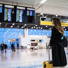 A woman with a suitcase looks at digital screens in an airport in Brazil