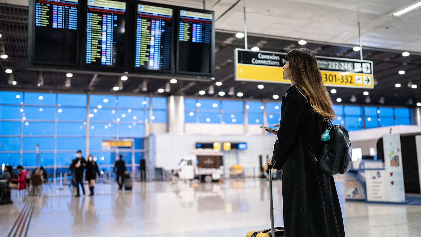 A woman with a suitcase looks at digital screens in an airport in Brazil