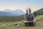 Two young women sitting on top of camper van in remote mountain landscape with arms raised in celebration © Tony Anderson / Getty Images