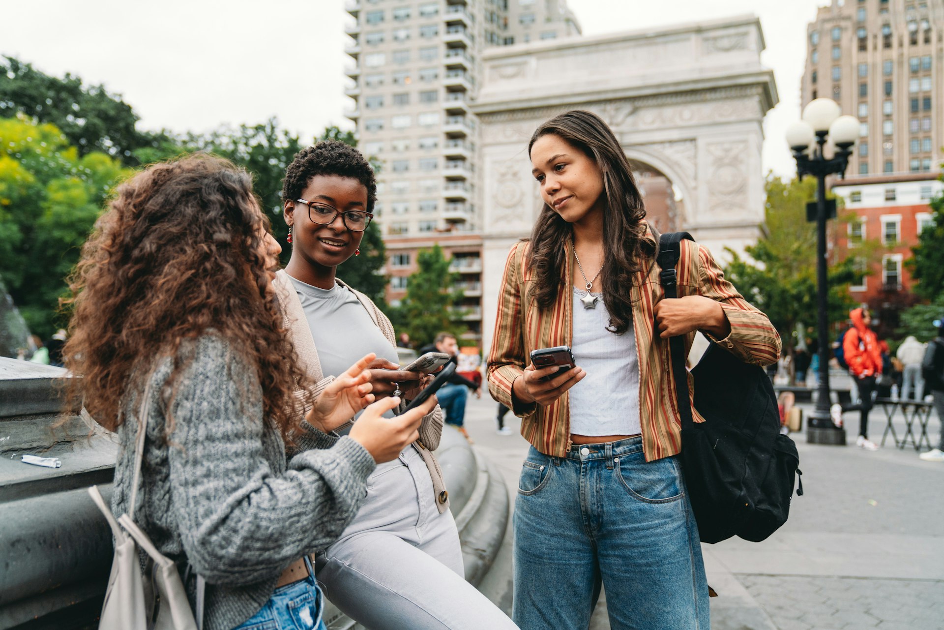 Three young women chatting by a fountain in Washington Square Park, NYC