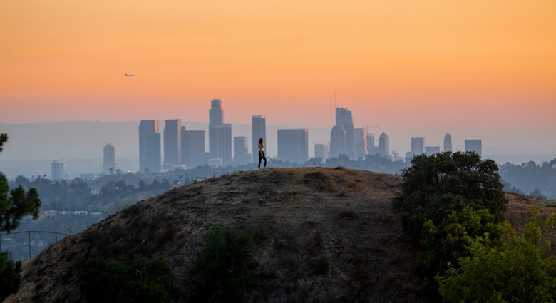 Woman standing on hill with Downtown Los Angeles cityscape in the background.
1444914619