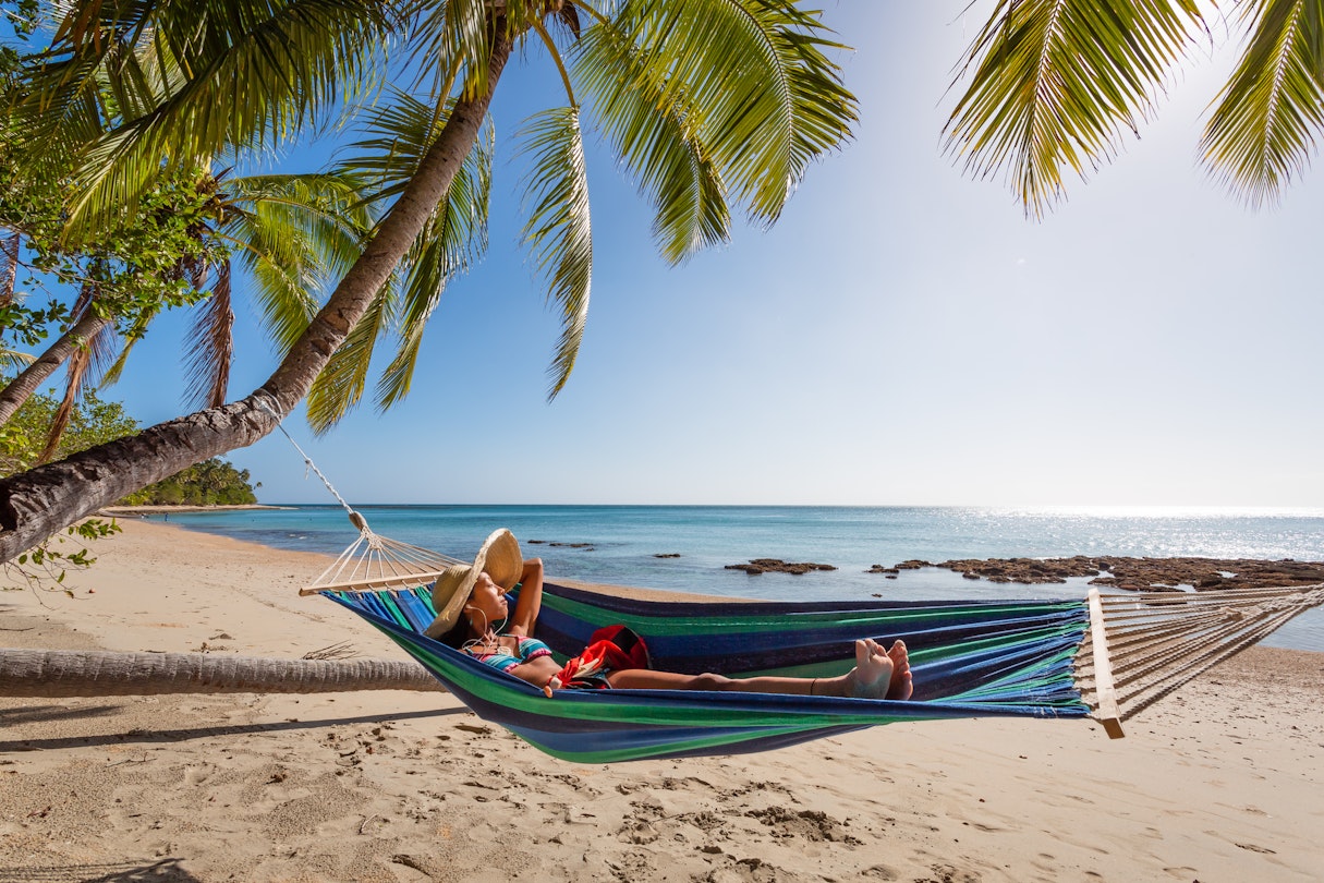 Woman with headphones lying on a hammock at the beach, Kadavu island, Fiji
