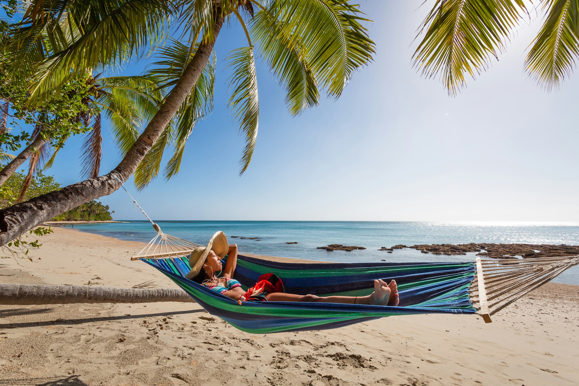 Woman with headphones lying on a hammock at the beach, Kadavu island Fiji