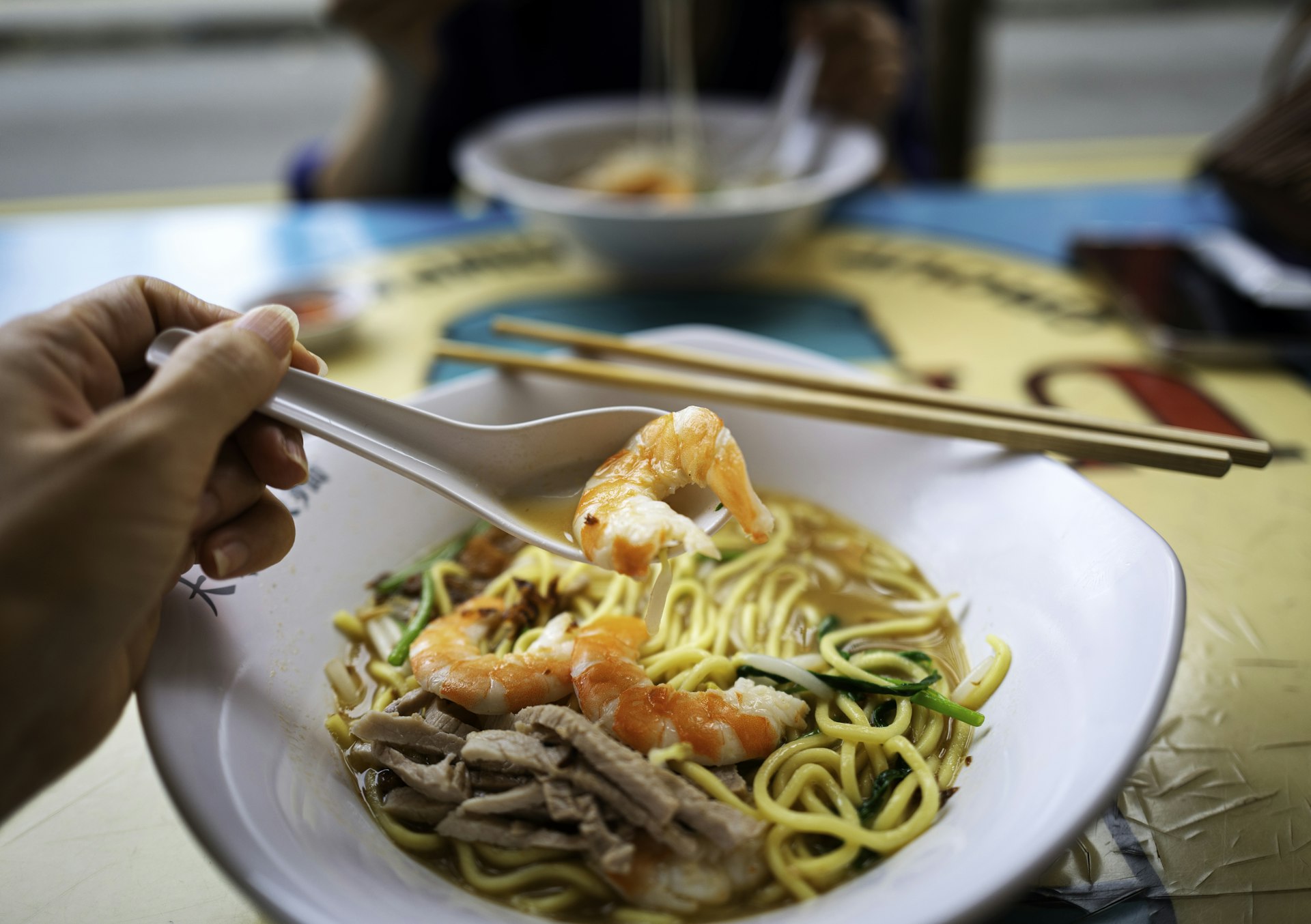 A person uses a spoon to eat a famous prawn noodle dish in Singapore