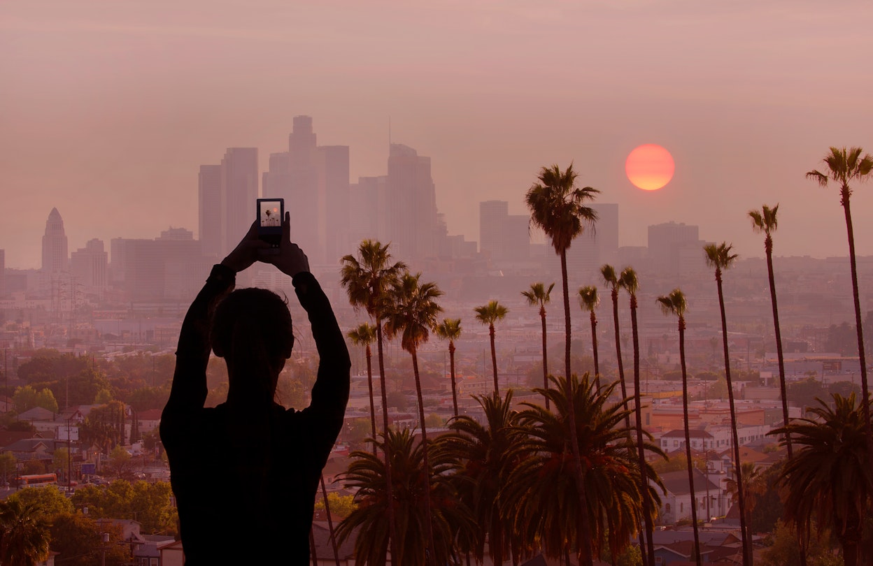 A woman takes a photo of the sunset in Los Angeles