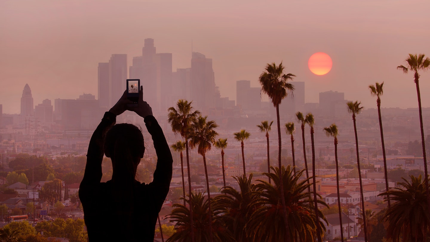 A woman takes a photo of the sunset in Los Angeles