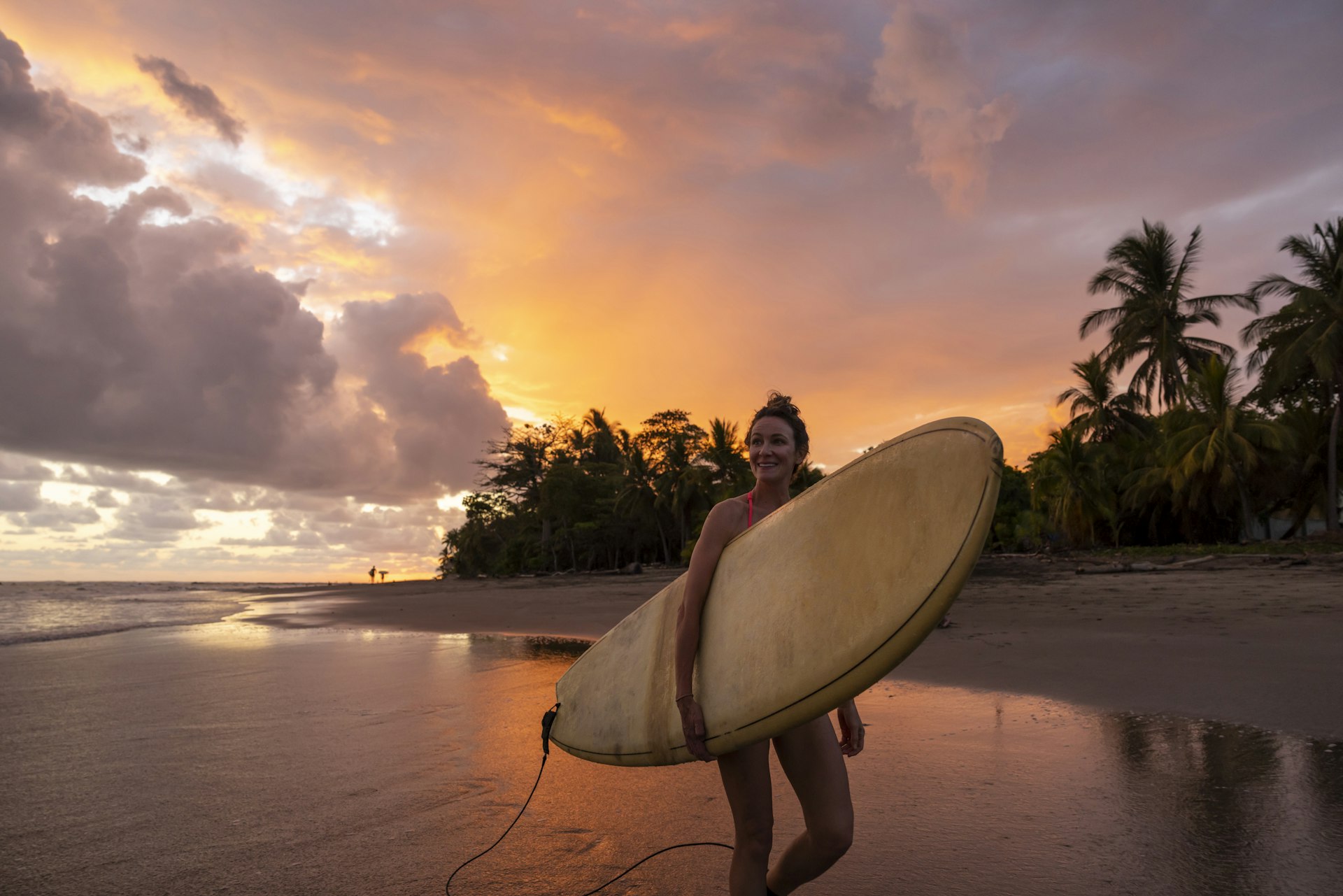A woman carries a surfboard on Playa Jaco at sunset