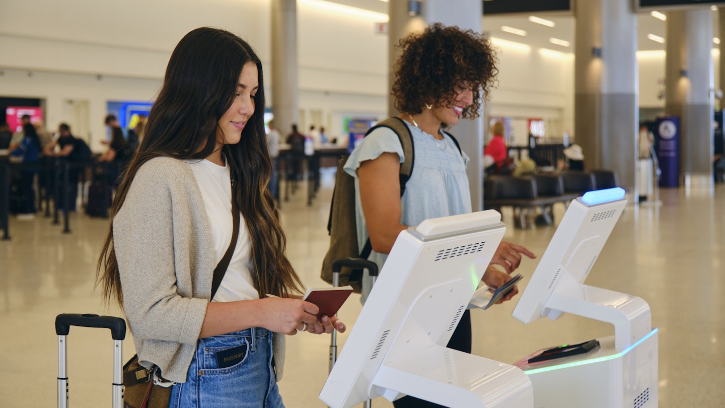 Two young women checking in at automated airport machines