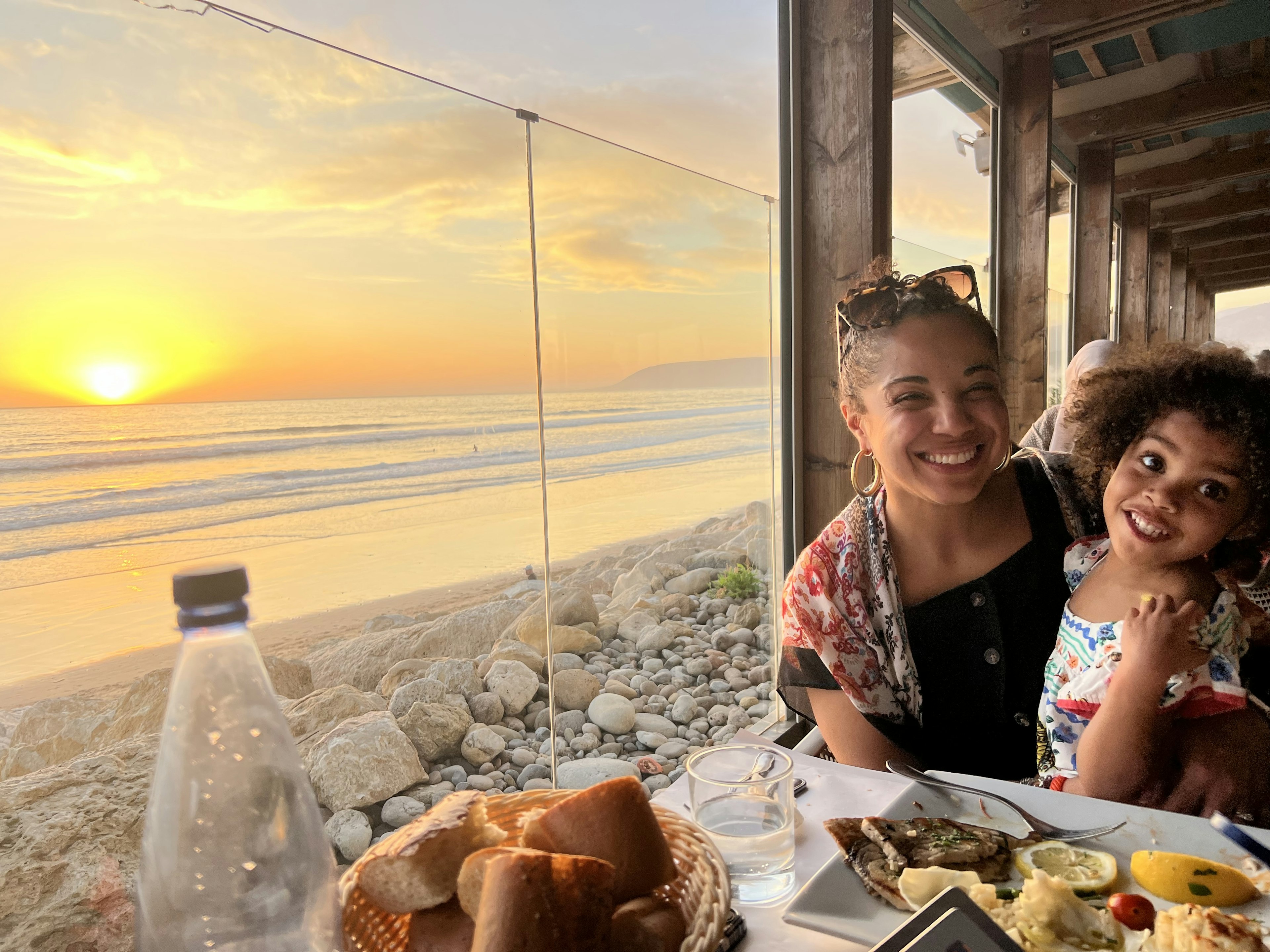 A woman and a child laugh while eating dinner at a seaside restaurant in Morocco