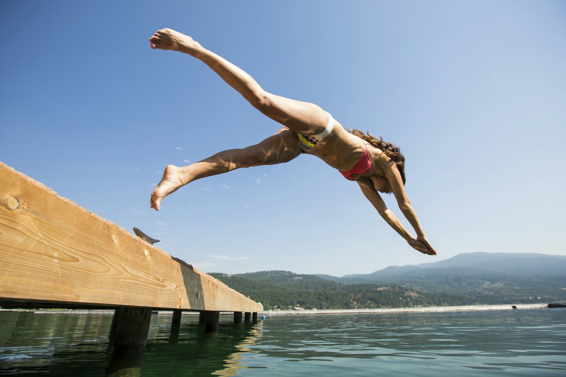 A woman jumps into the clear water of Flathead Lake from a small dock.