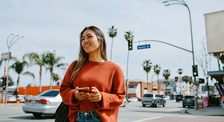A young woman standing on a street in LA holding her phone.