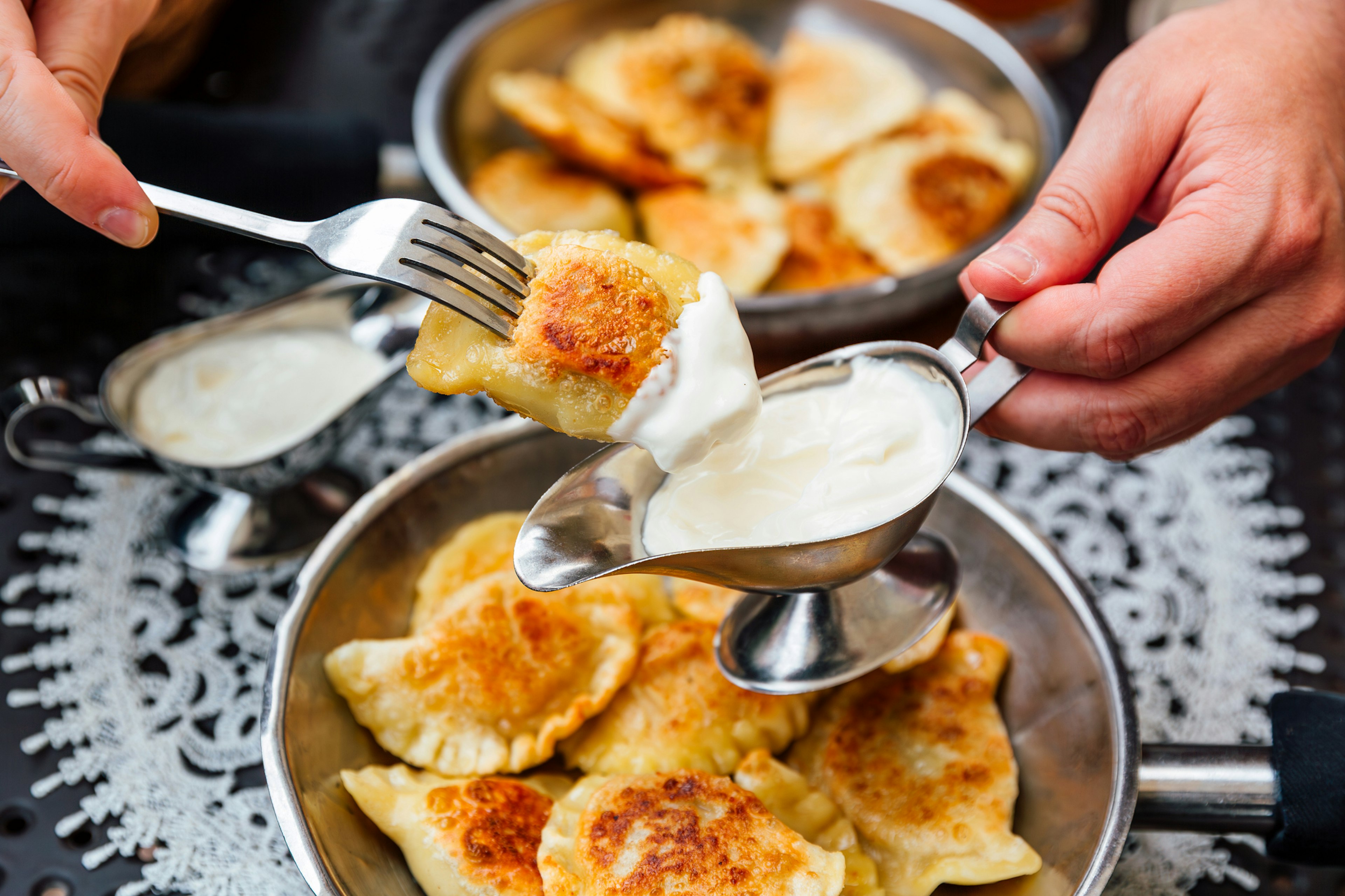 A person dipping Polish pierogi in sour cream