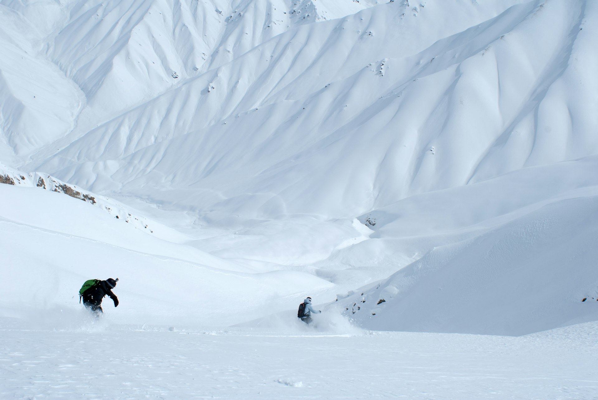 Two skiiers carve paths through a mountainous wilderness area in Uzbekistan