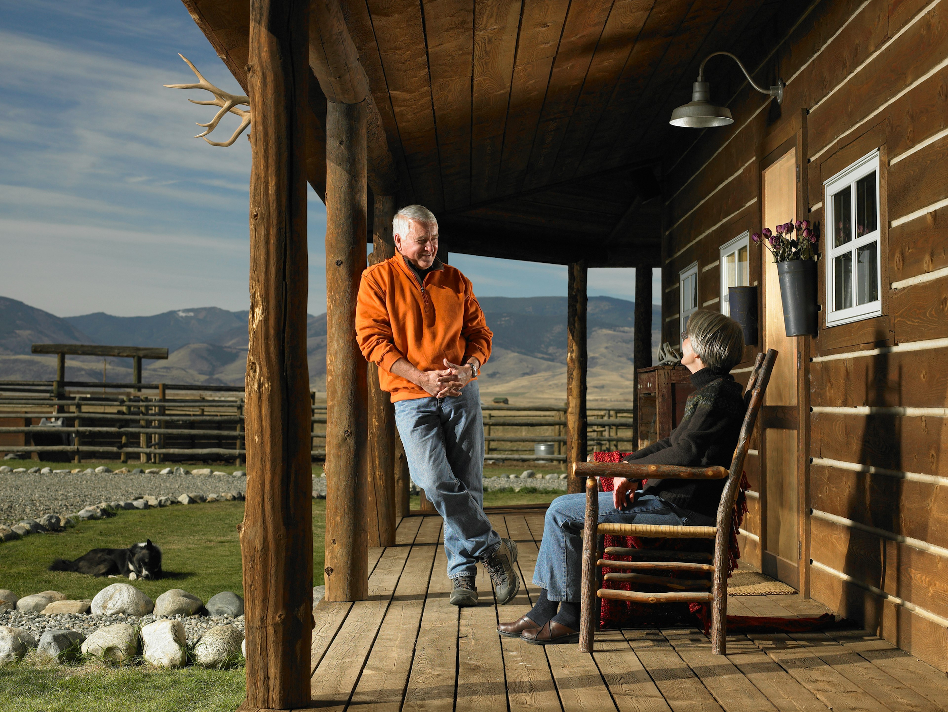 A senior couple smile on the porch of a wooden cabin