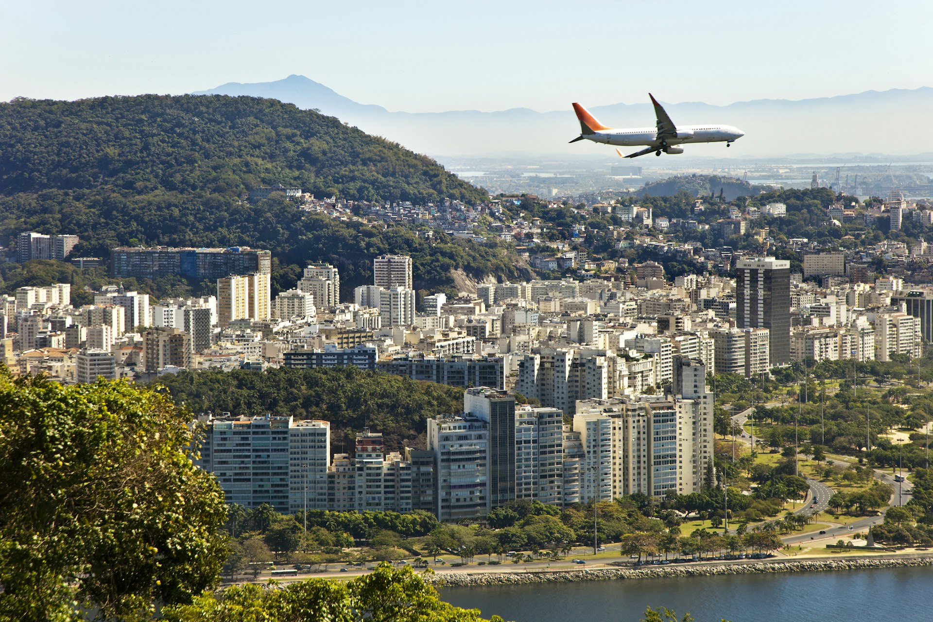 A commercial jet flies over a built-up city by the sea 