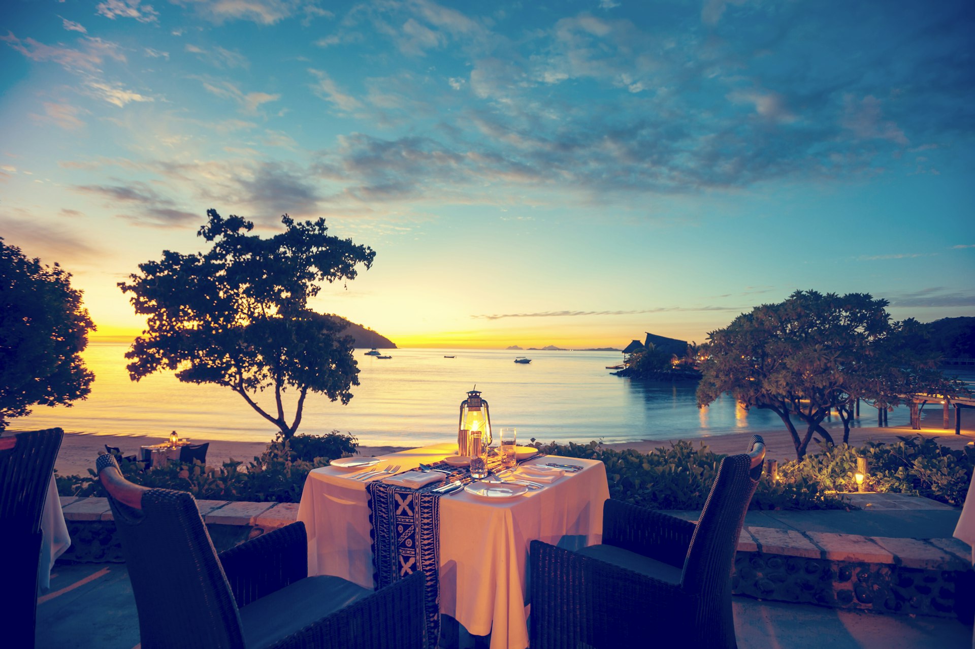 An outdoor table at a restaurant overlooking the ocean as the sun sets