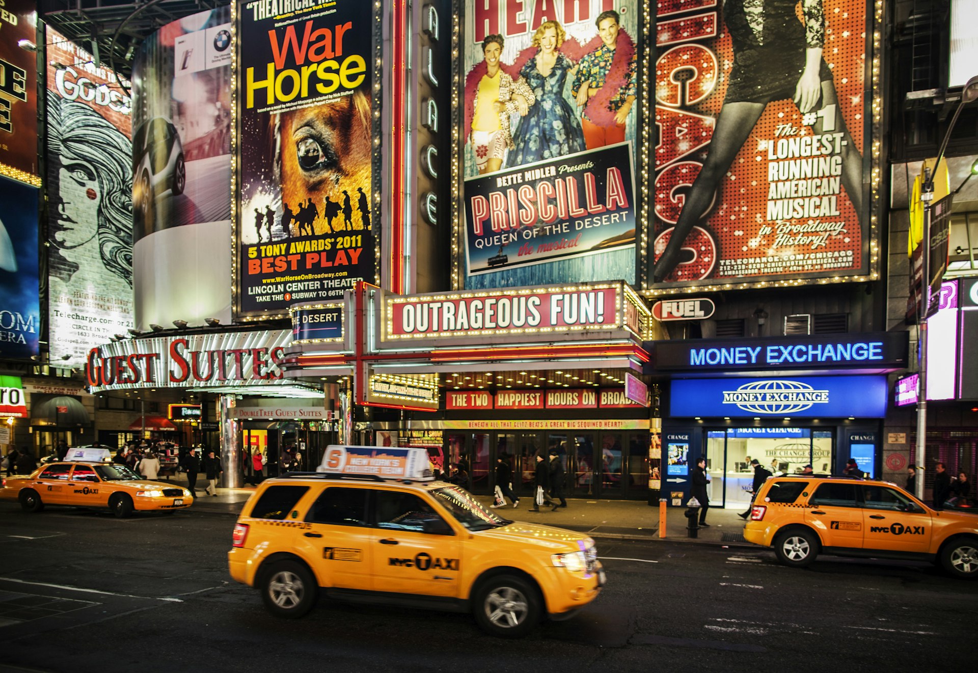 Broadway theatres in Times Square New York city with big billboards showing adverts at night with taxis stood out front