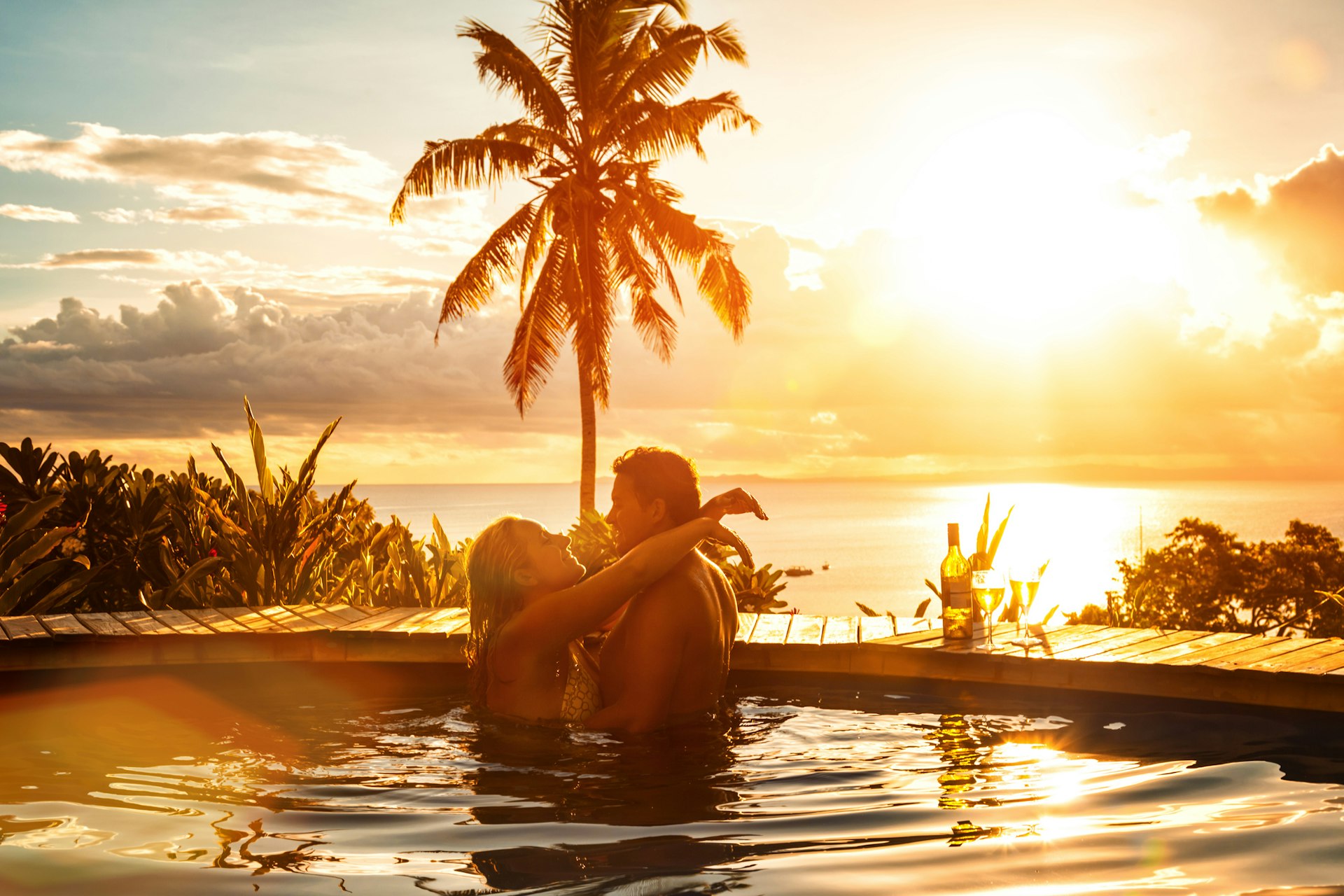 A couple embracing in the pool in Fiji as the sun sets behind them