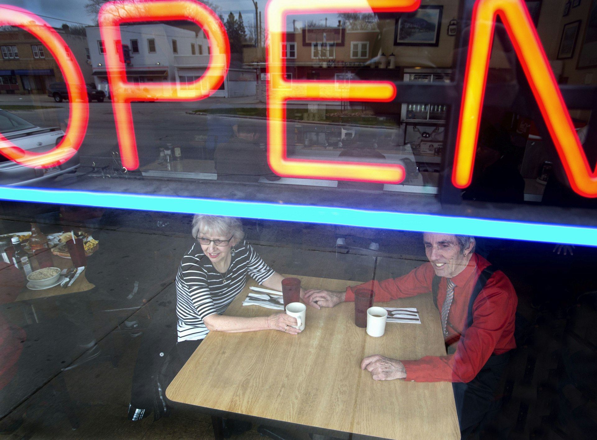 A couple holds hands at a diner table while looking out the window under an open sign at a diner in Milwaukee, Wisconsin